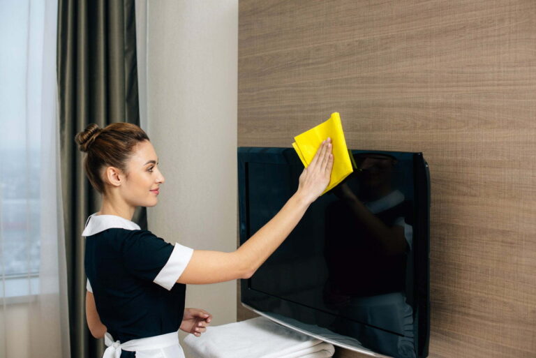young beautiful maid in uniform cleaning tv screen with rag