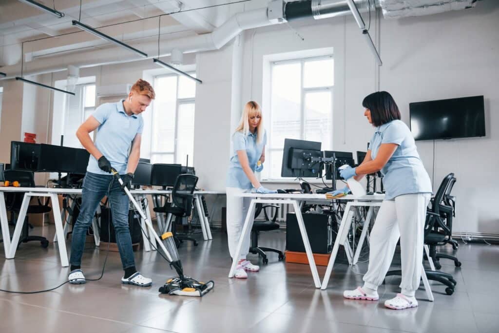 Cleans floor. Group of workers clean modern office together at daytime